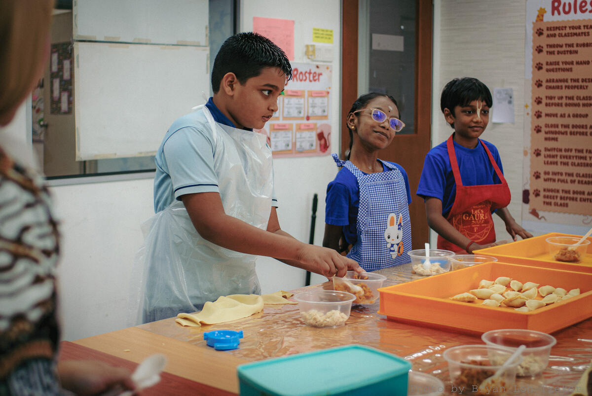 Pupils folding curry puffs onto a tray at Edusky's Merdeka celebration