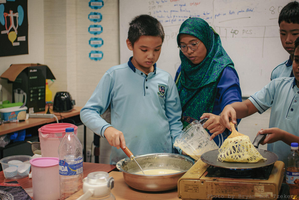 Hands folding curry puffs on a tray for Merdeka