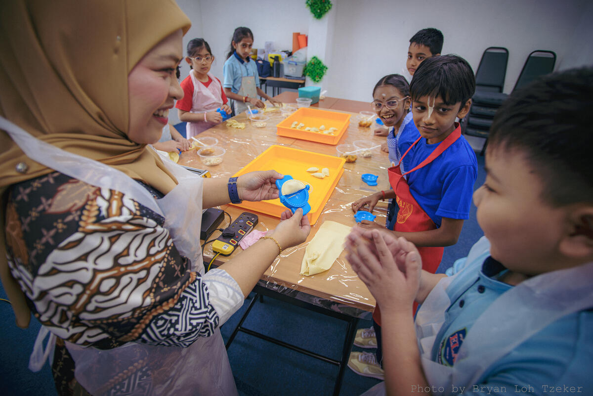 Pupils stirring a pot together for Merdeka cooking