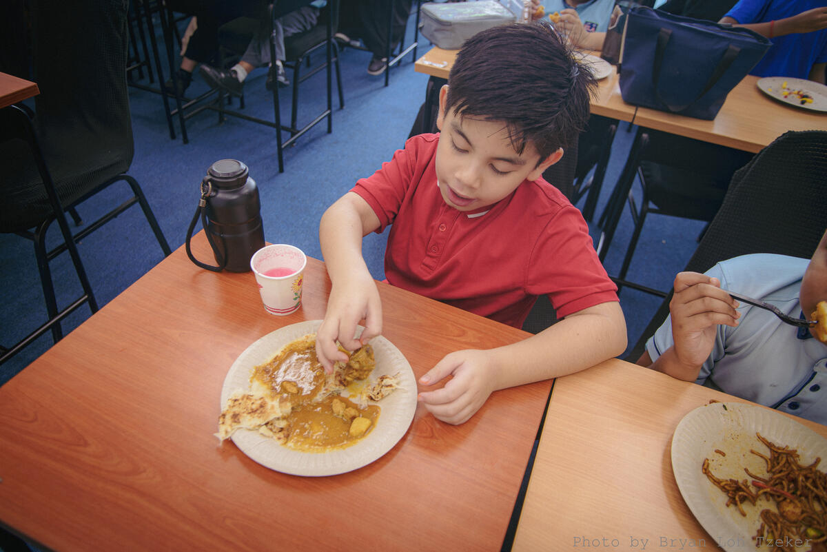 Pupils enjoying curry puffs at the Merdeka feast