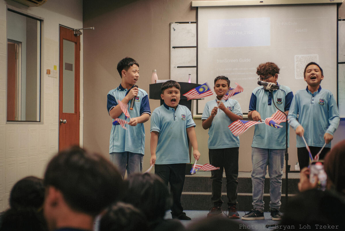 Pupils singing together on stage for Merdeka